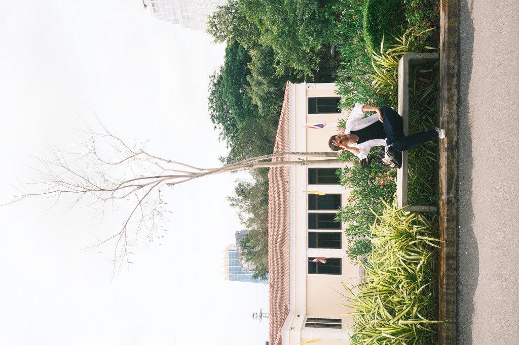 Harris sitting on a bench outside a building surrounded by greenery.