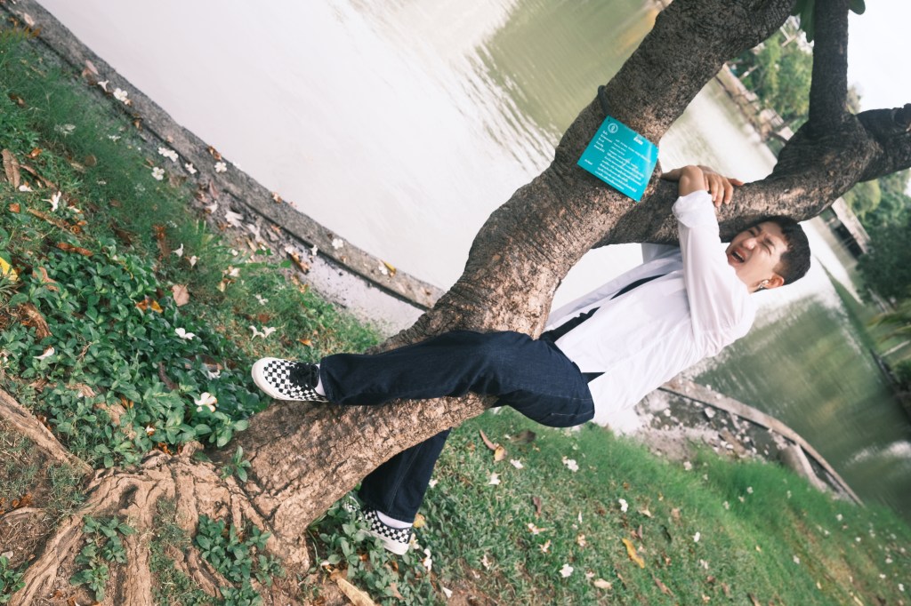 clinging to a tree beside a pond, eyes squeezed shut and mouth open.